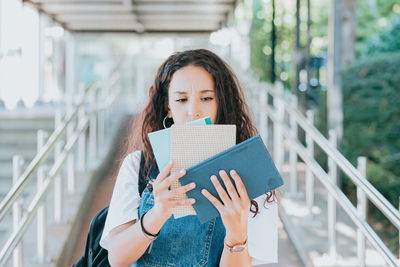 Portrait of young woman holding book while standing outdoors