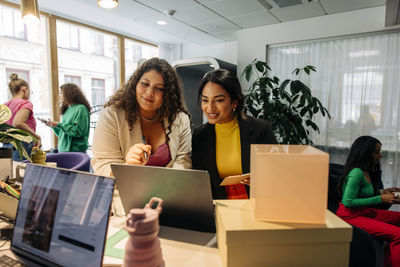 Smiling female entrepreneurs discussing over laptop while working at office