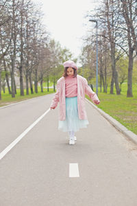 A little charming girl walks along an asphalt road in the park.