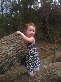 Close-up of girl standing fallen tree in forest