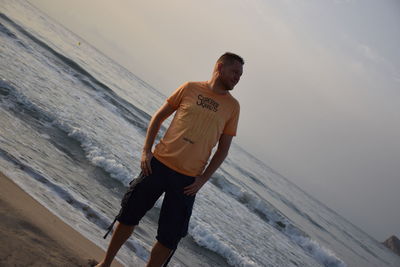 Young man standing on beach against sky