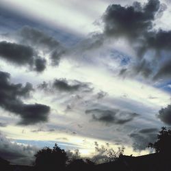 Low angle view of silhouette trees against cloudy sky