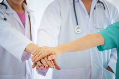 Midsection of doctors stacking hands while standing against white background