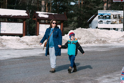 Full length of mother and son holding hands while walking on road during winter