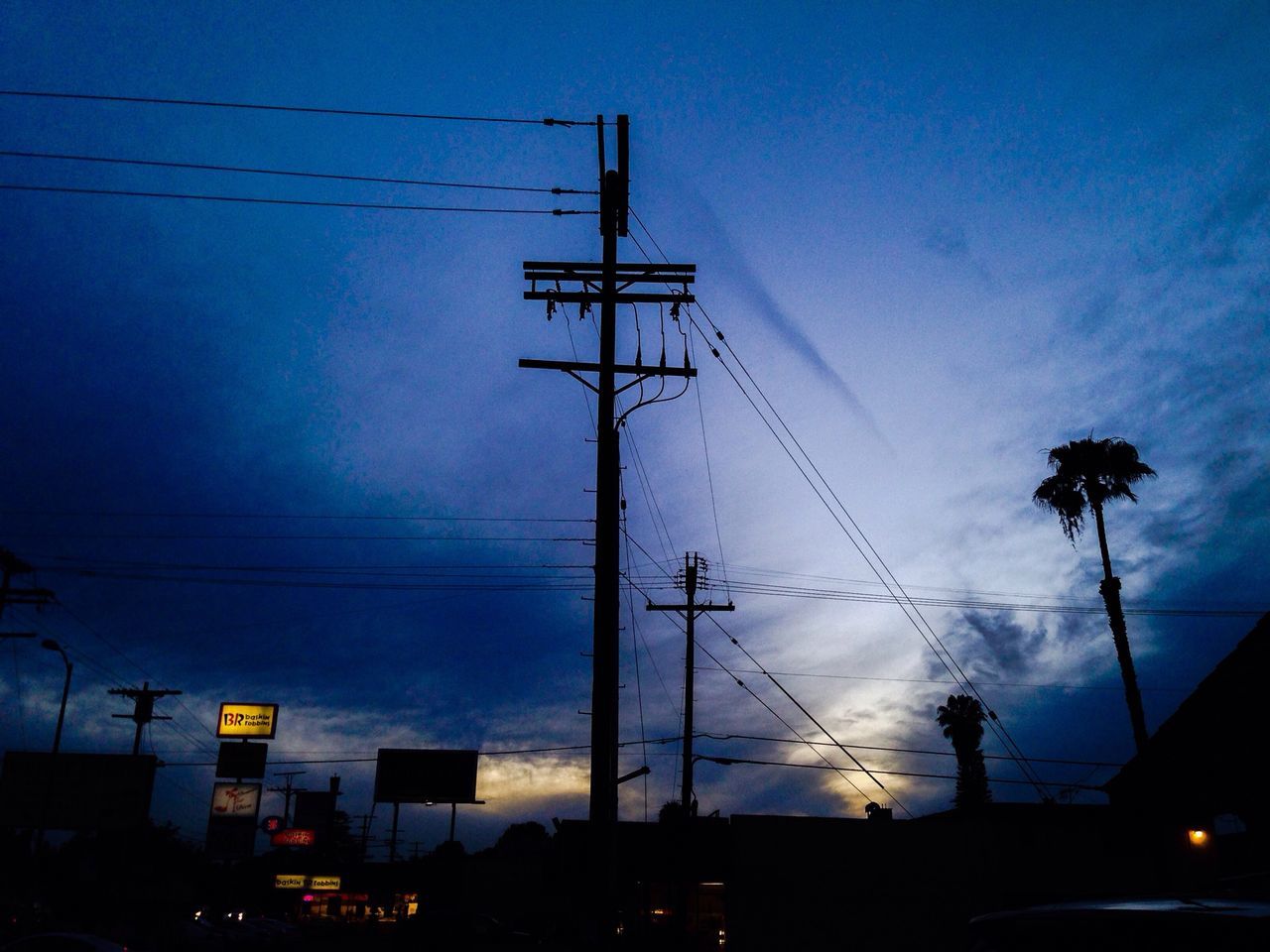 power line, electricity pylon, electricity, power supply, cable, sky, low angle view, connection, silhouette, building exterior, fuel and power generation, technology, built structure, power cable, architecture, street light, dusk, city, blue, illuminated