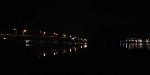 Illuminated city by river against sky at night