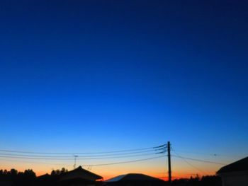 Silhouette electricity pylons against clear blue sky