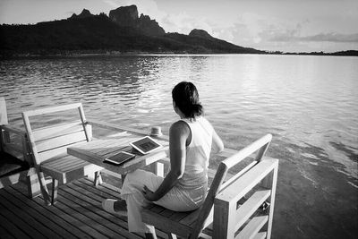 Rear view of woman sitting on pier at lake