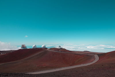 Winding road amidst desert against blue sky during sunny day