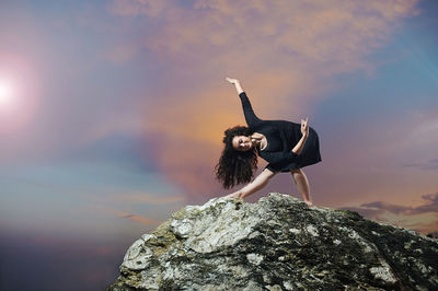 Woman standing on rock against sky during sunset