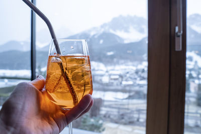 Close-up of hand holding drink against mountains at resort during winter