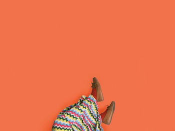 Low section of woman wearing shoes against orange background