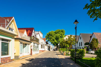 Street amidst houses and trees against clear blue sky