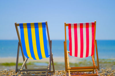 Deck chairs on beach against clear blue sky