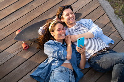 Top view of man and woman with skateboard watching video or photos on smartphone