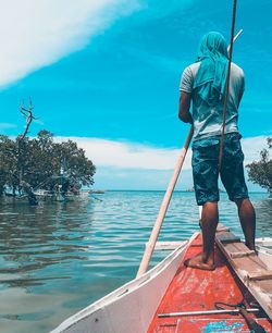 Rear view of man standing in boat on sea against sky