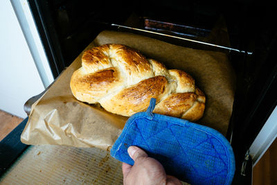 Cropped image of person taking braided bread from oven