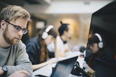 Male programmer working on computer with colleagues at desk in office