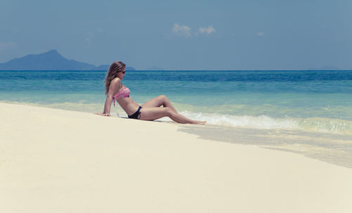 Woman sitting on beach against sky