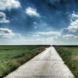 Road passing through field against cloudy sky