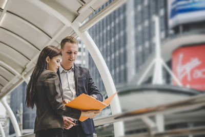 Low angle view of colleagues discussing file while standing on footbridge