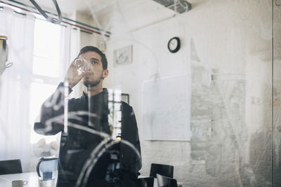 Creative businessman seen through glass while drinking water in board room