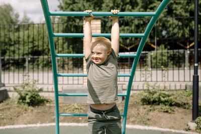 Smiling boy with down syndrome hanging from jungle gym at park