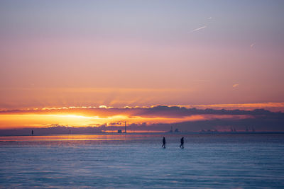 Silhouette people on sea against sky during sunset