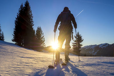 Rear view of mature man skiing on snow covered landscape against blue sky during sunset
