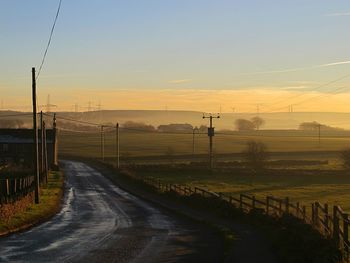 Road amidst field against sky during sunrise