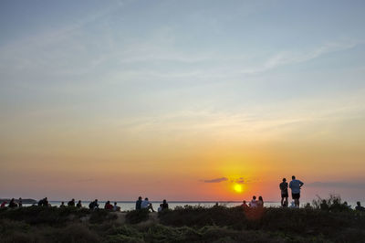 People standing on land against sky during sunset