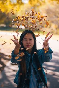 Portrait of woman throwing dry leaves on footpath