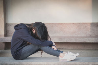 Woman sitting on staircase against wall