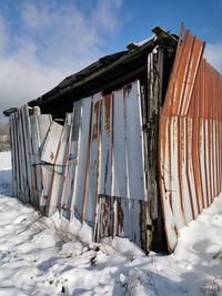 Abandoned house on snow covered field against sky