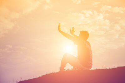 Side view of man sitting against sky during sunset