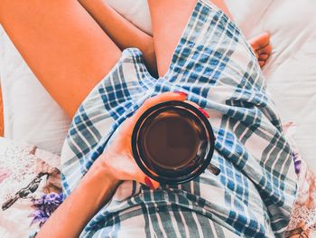 Low section of woman drinking coffee on bed