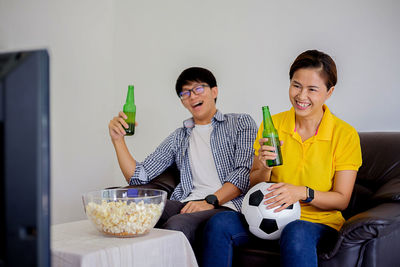 Smiling friends watching sport while having food and drink at home