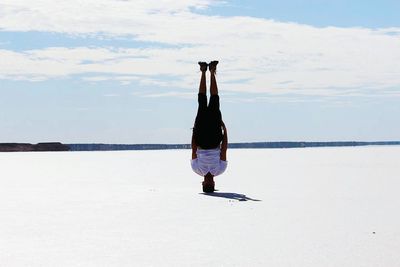 Full length of man doing headstand on salt flat against cloudy sky