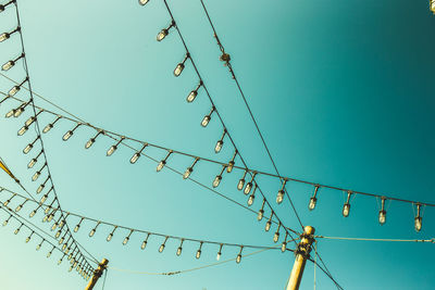 Low angle view of lights hanging against clear blue sky