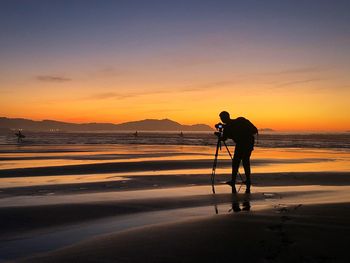 Silhouette man standing on beach against sky during sunset