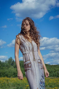 Woman with tousled hair standing on field against sky