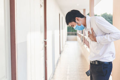 Side view of man wearing mask coughing while standing at balcony