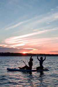 Silhouette people in boat against sky during sunset