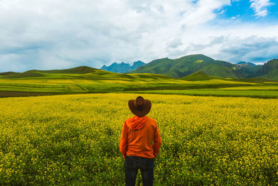 Rear view of man standing amidst flowering plants on field