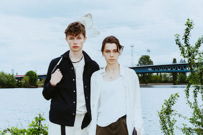 Portrait of young friends collecting plastic garbage near river against sky