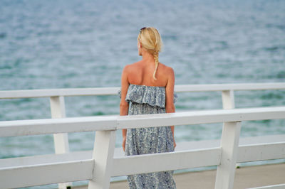 Rear view of young woman standing on pier over sea