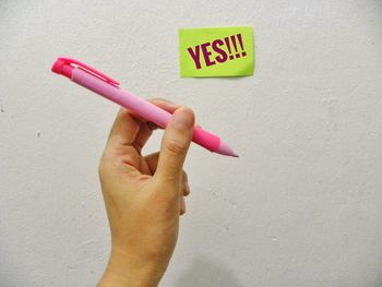 Cropped hand holding pen by adhesive note with yes text on wall