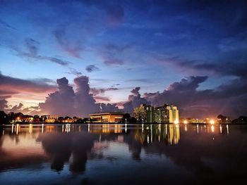 Illuminated buildings by lake against sky during sunset