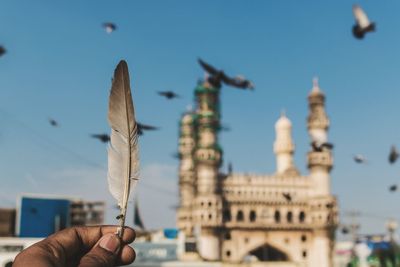 Cropped hand of man holding feather against char minar