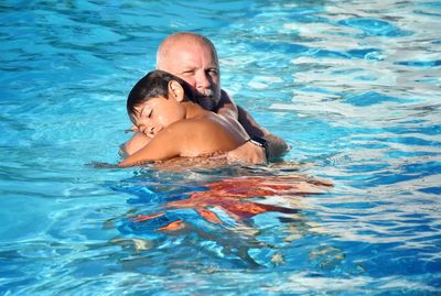 Father embracing shirtless son while swimming in pool
